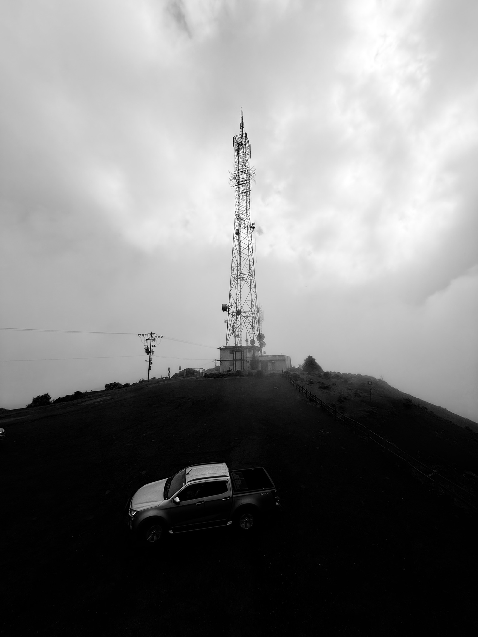 Torre de telecomunicaciones entre niebla, con un vehículo al pie de la ladera.