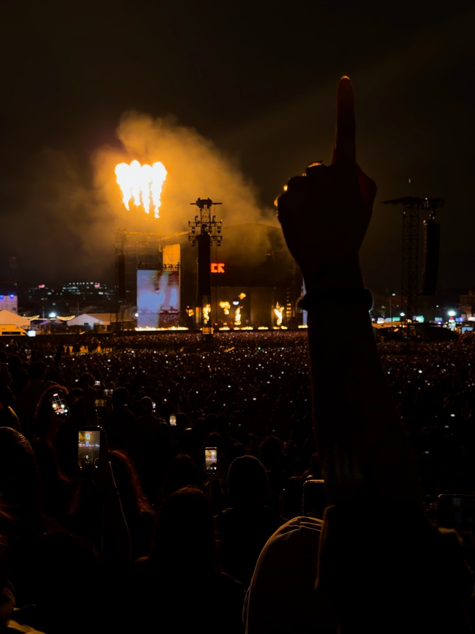 Una mano levantada frente a un escenario de concierto iluminado por fuego.